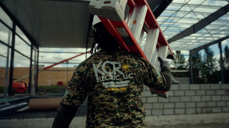 A man holding a ladder in a KCR Electric Shirt